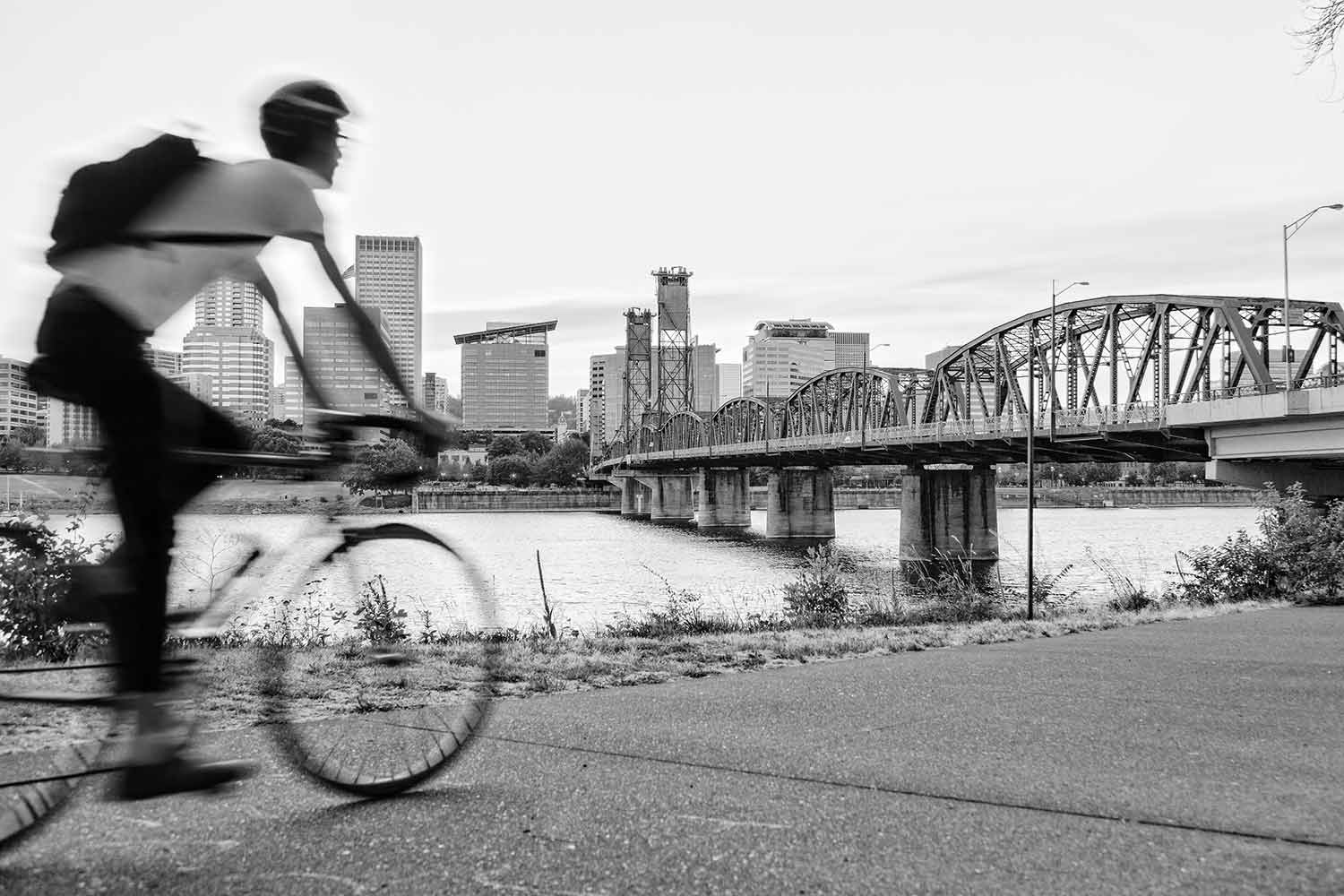 Man riding bike in Portland, OR near the water, overlooking the skyline.